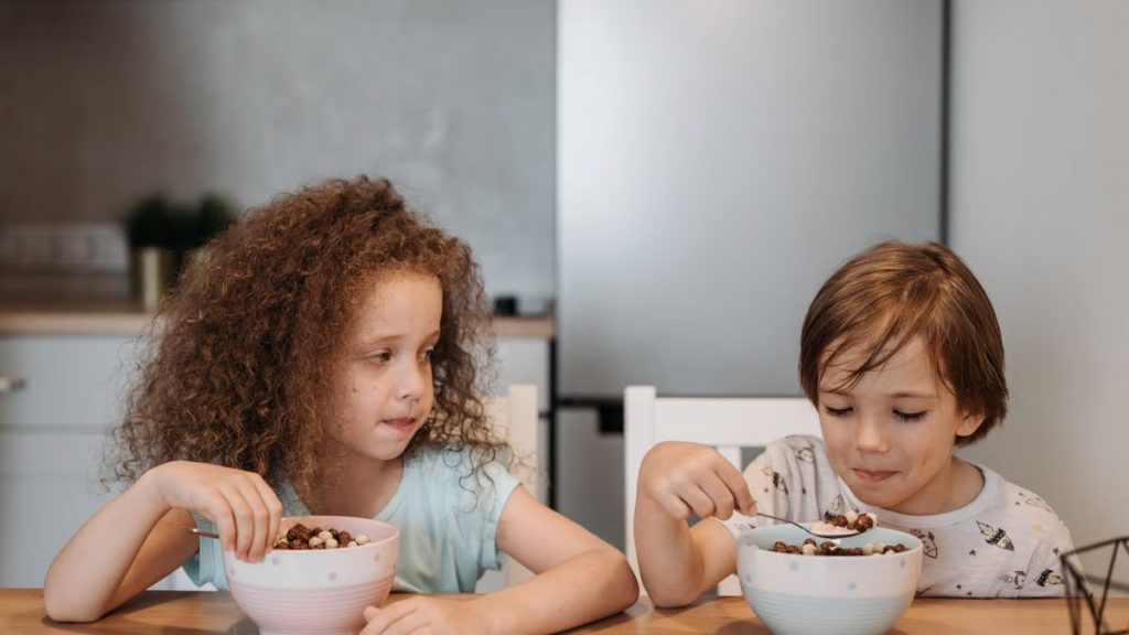 Two children enjoying breakfast cereal at a cozy kitchen table.