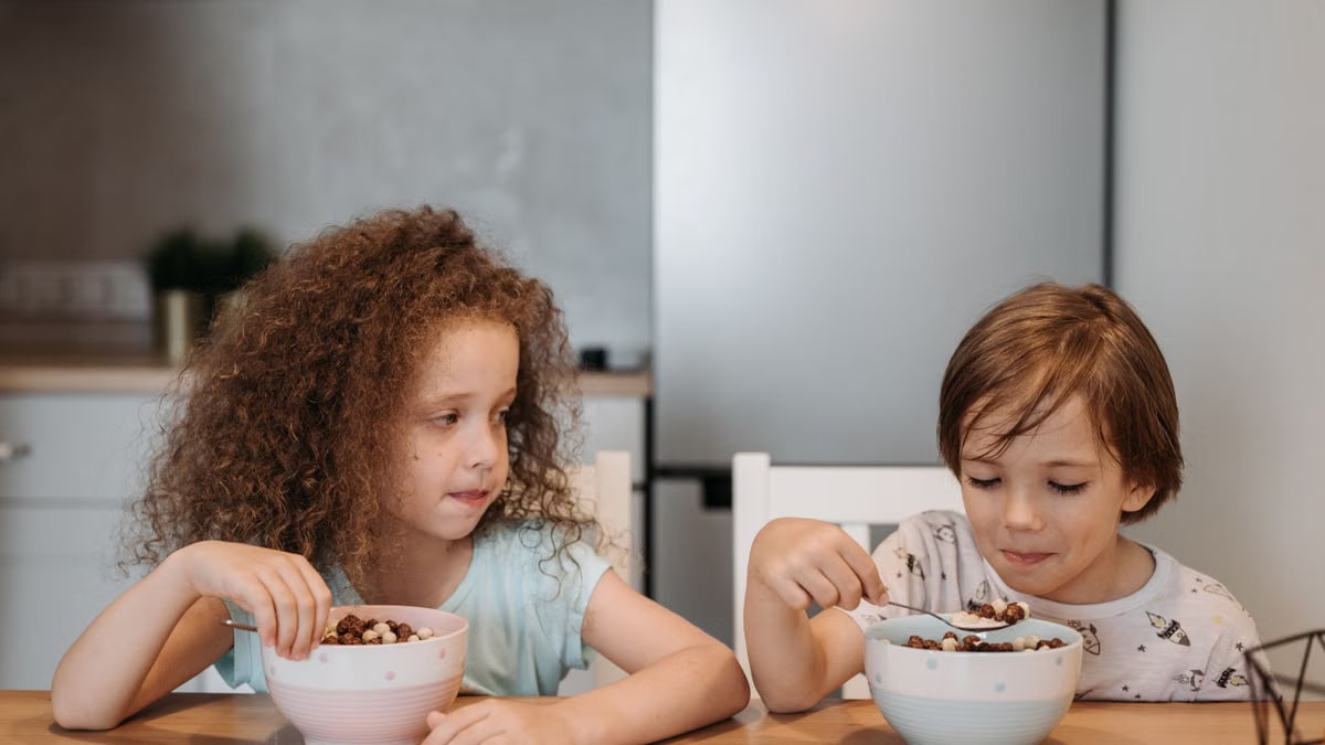 Two children enjoying breakfast cereal at a cozy kitchen table.